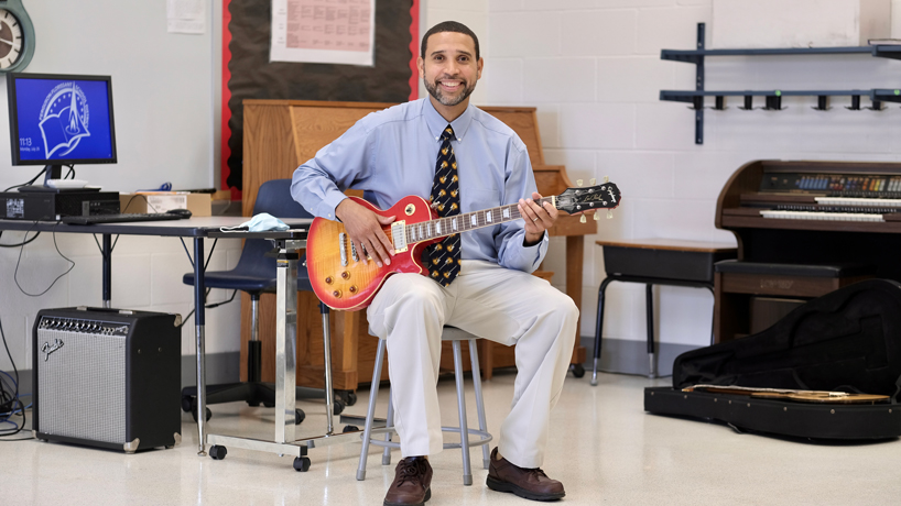 James Young sits with guitar in his classroom