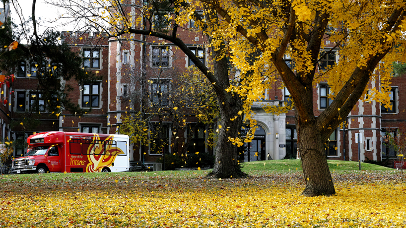 A shuttle bus pulls away from the Pierre Laclede Honors College as colorful leaves fall to the ground on a recent fall day