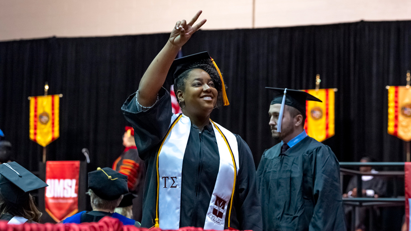 A student signals to her family members after walking across the stage during commencement