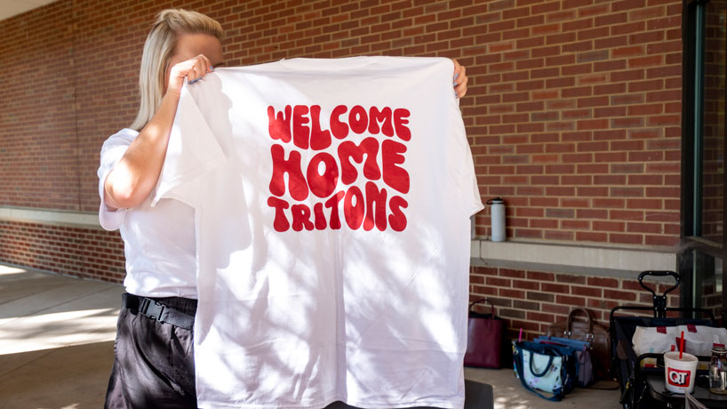 Woman holds up tee-shirt to welcome students to UMSL