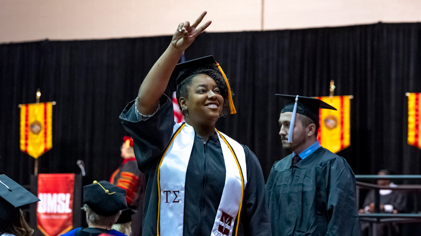 A graduating student flashes a peace sign to the crowd during commencement