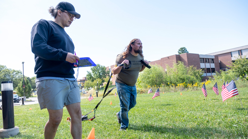 Robert "Otto" Ottinger drags a sled across the lawn outside the Recreation and Wellness Center during the UMSL Combat Fitness Test as Joseph Kalter grades his performance.