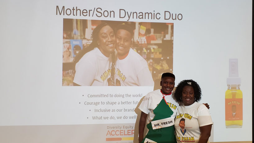 A 13-year-old boy stands with his mother in front of a screen with their photo on it.