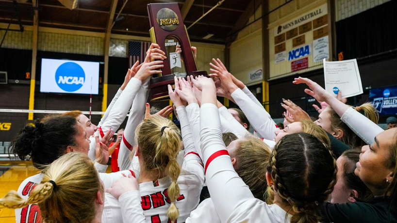 UMSL volleyball players gather together and hold up their regional championship trophy