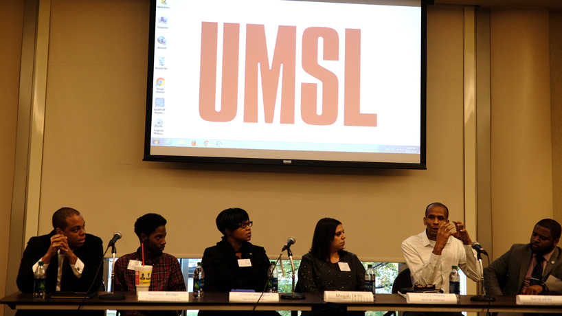 Local politicians are lined up behind a table as they take part in a panel discussion for the "ABC & Politics" event. A screen over their head in the Millennium Student Center Century Rooms reads UMSL.