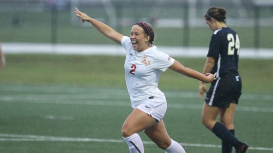 Miriam Taylor runs with her arms spread wide in celebration while a Rockhurst player walks with her head down after Taylor scored a goal.