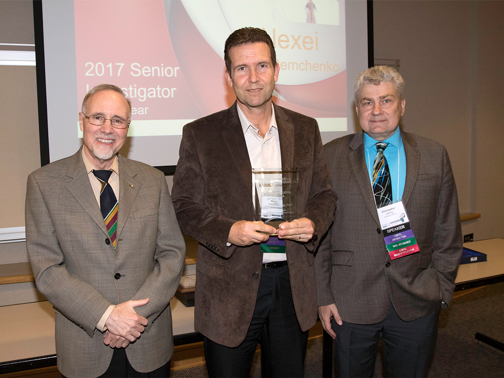 Chancellor Tom George (at left) and Vice Provost of Research Chris Spilling (at right) present Alexei Demchenko with UMSL's 2017 Senior Investigator of the Year award last month at a ceremony concluding Research and Innovation Week on campus. (Photo by August Jennewein)