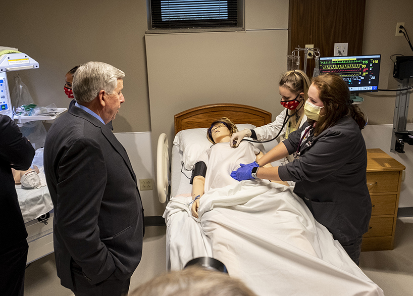 Gov. Mike Parson (left) observes two UMSL BSN students as they demonstrate how learning works in the new College of Nursing Simulation Labs.