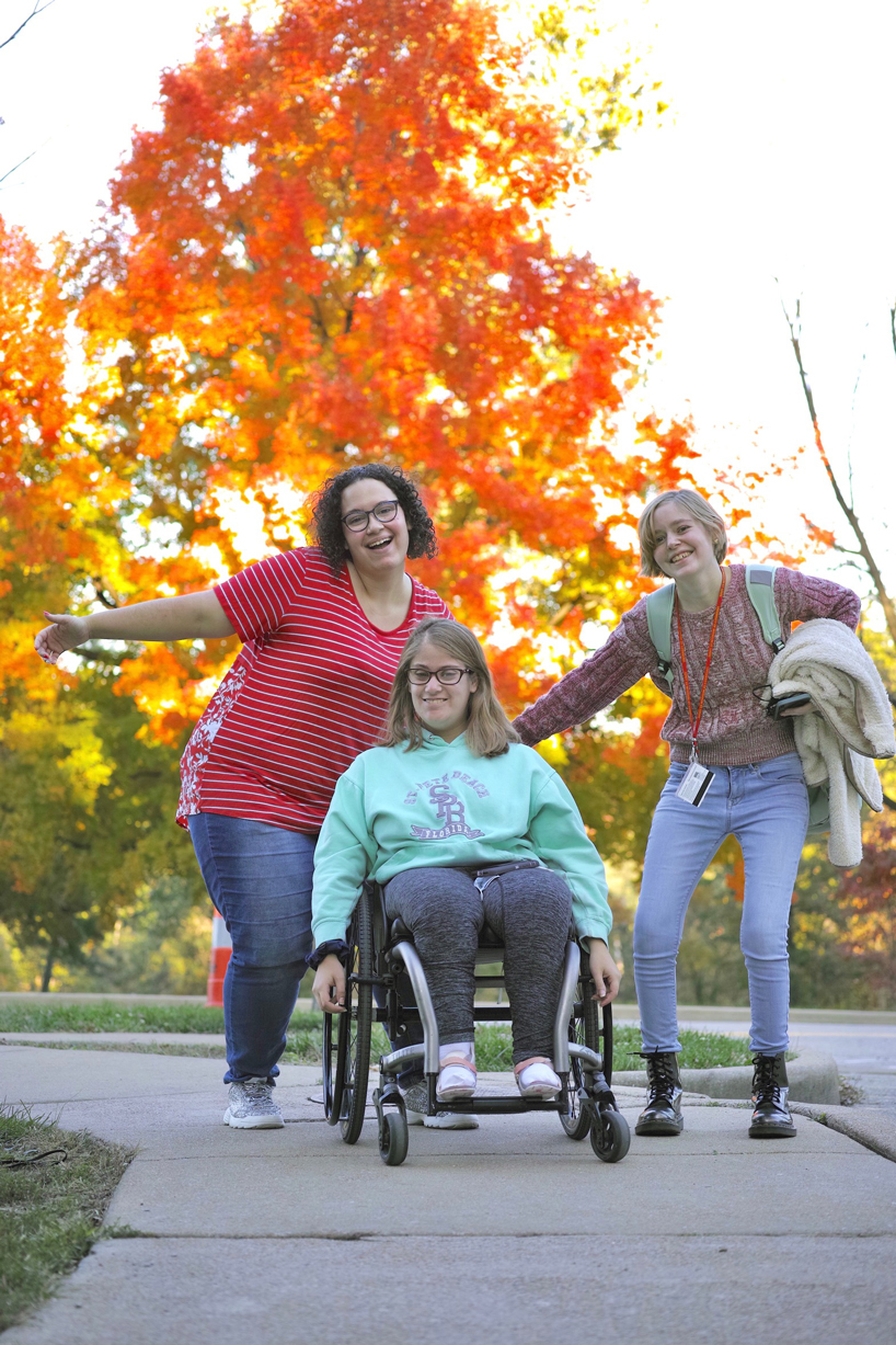 UMSL Succeed students Destiny Trent, Brooke Clemons and Sophia Epps smiling together in front of fall tree
