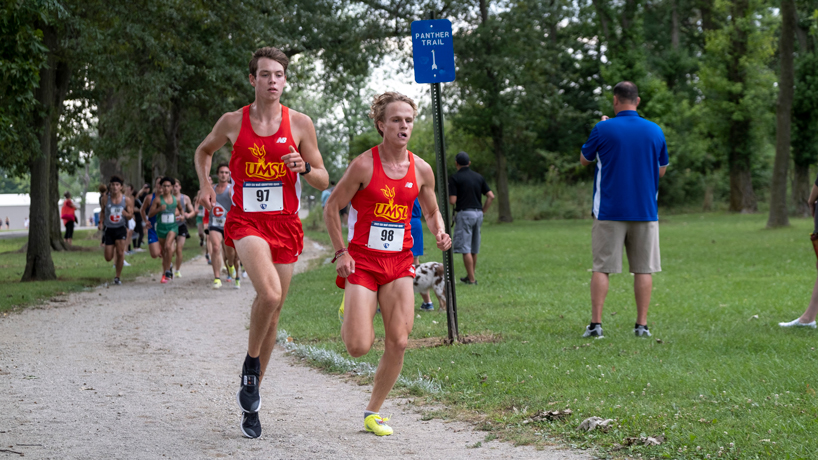 Cross country runners Benjamin VandenBrink and Jacob Warner run side-by-side and ahead of a pack