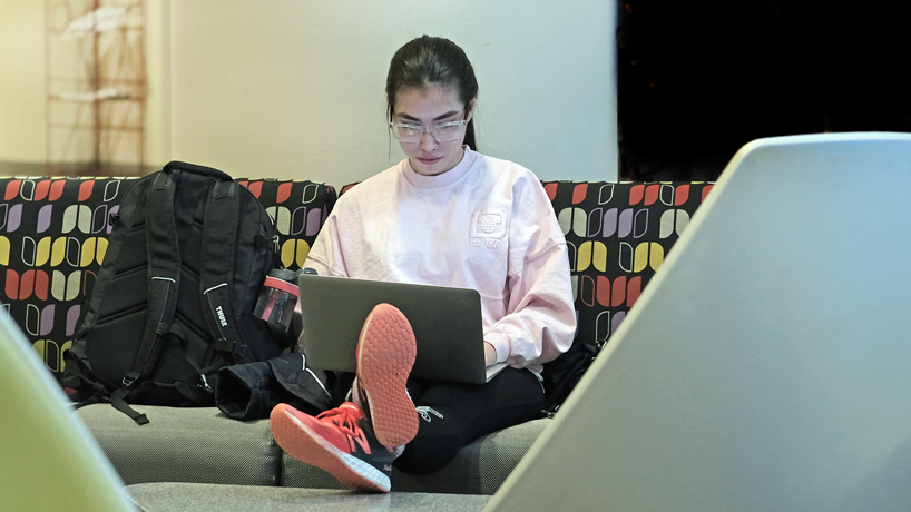 A student sits on a couch and works on her laptop