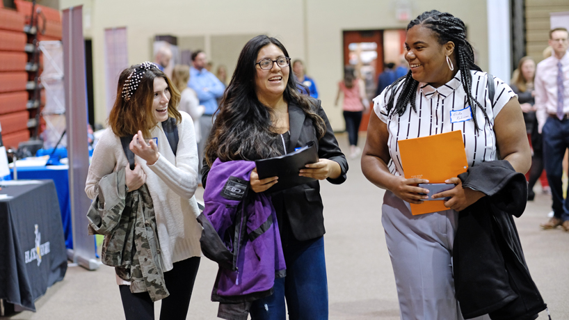 Three young women chat while at a job fair.