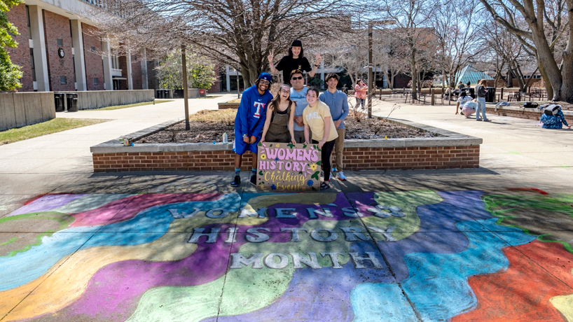Students stand in the Quad on brightly colored chalk art 