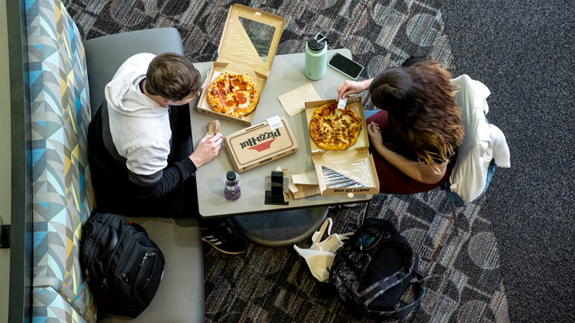 Overhead photo of students sitting together with pizza at a table in The Nosh