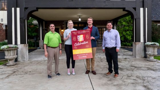 Staff and Board members of the UMSL Alumni Association stand outside a country club while the middle two hold a sign about the new alumni event