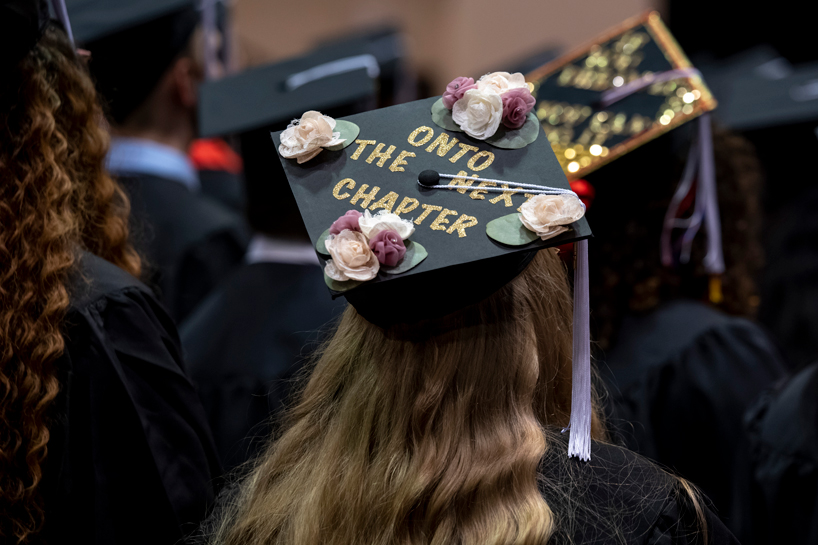 A student wears a graduation cap decorated with the words "Onto the Next Chapter"
