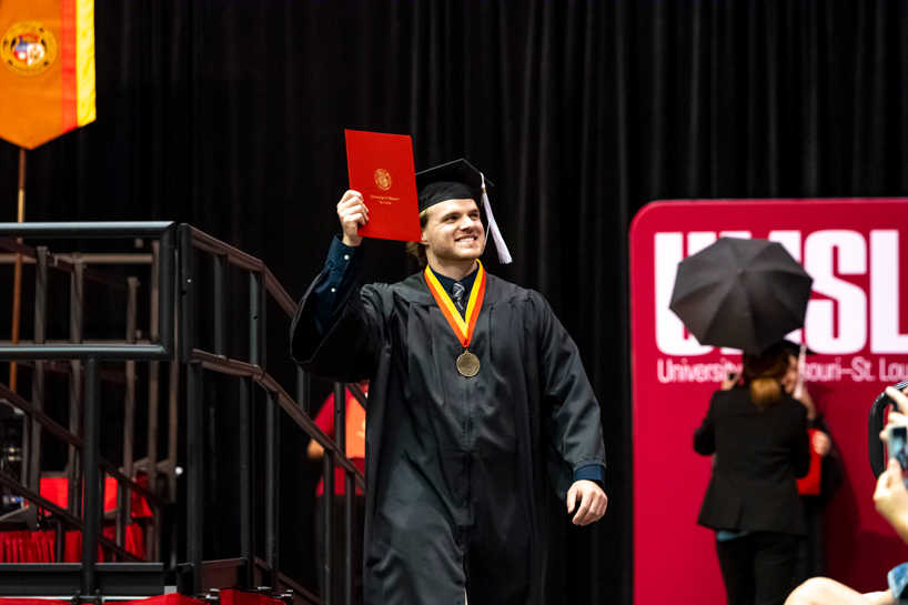 A student holds up his diploma after walking across the stage during commencement