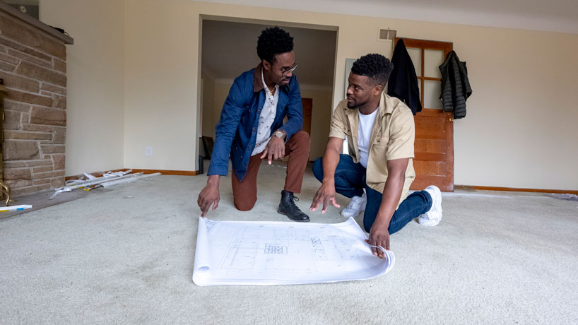 Two brothers kneel on the floor looking at blueprints