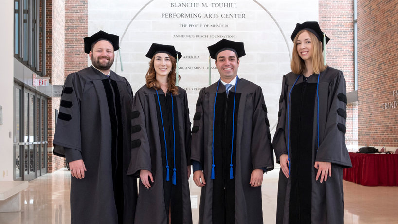 Four graduates stand in their caps and gowns.