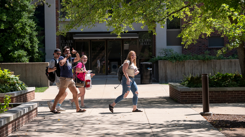 Students pointing toward camera as they walk through Quad on a summer day