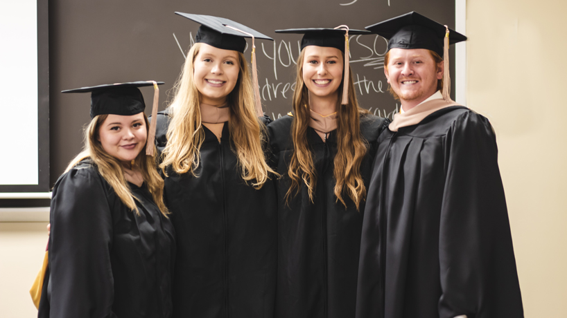 Four students stand in their caps and gowns.