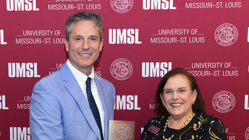 A man in a blue suit receives an award from a woman standing next to him.