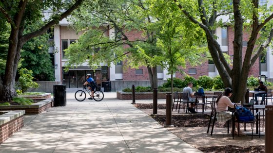 A police officer rides his bike through the Quad as students study outdoors