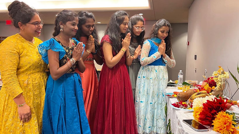 Indian women dressed in cultural clothing are standing, praying to a god.