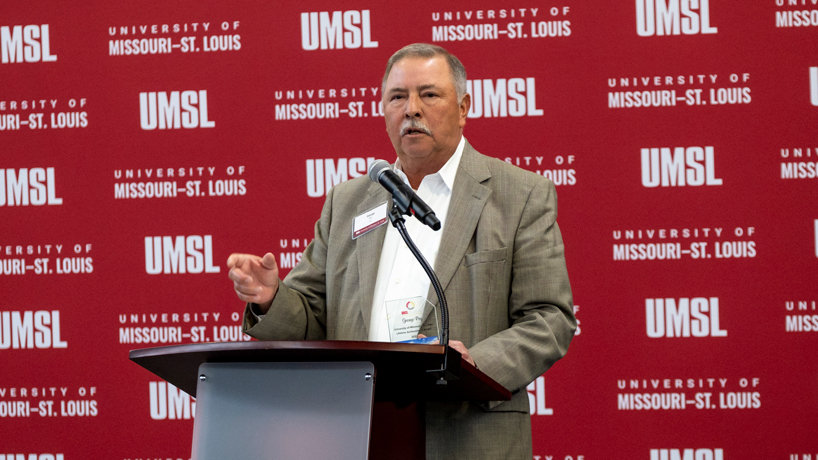 George Paz speaks at a lectern with an UMSL backdrop behind him