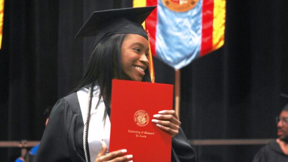 A student smiles after walking across the stage and receiving her diploma holder