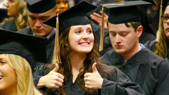 A new graduate holds up two thumbs as she looks into the audience during commencement
