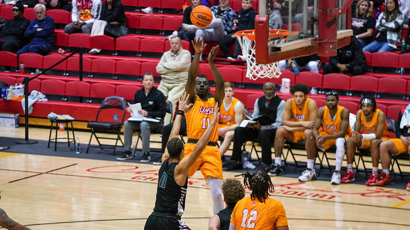 Basketball player Isaiah Fuller take a jump shot from the wing with the UMSL bench behind him