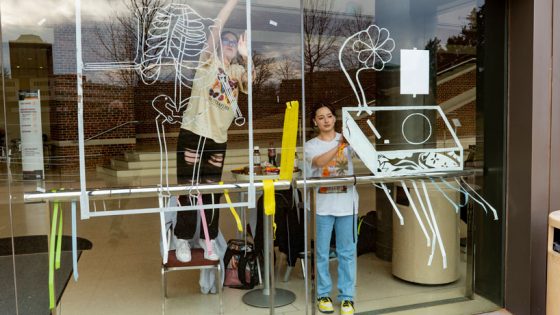 Visual arts students create artwork on the windows of the Touhill lobby out of tape.