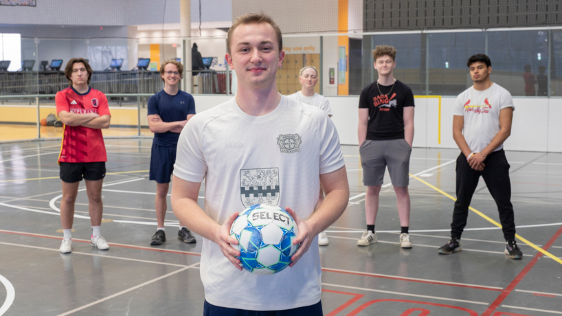 Tritons Football Club president Alexander Orywall holds a soccer ball in the foreground while other club members stand behind him in the background