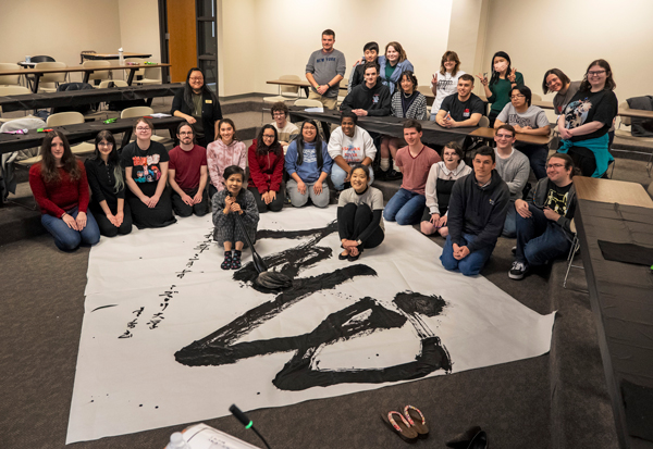 Kaori Ishijima and Hiroko Yoshii and Japanese students sit at the edge of Ishijima's large scale calligraphy drawing of the spring letter