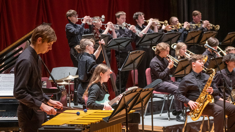 A jazz band of students play on stage in an auditorium.