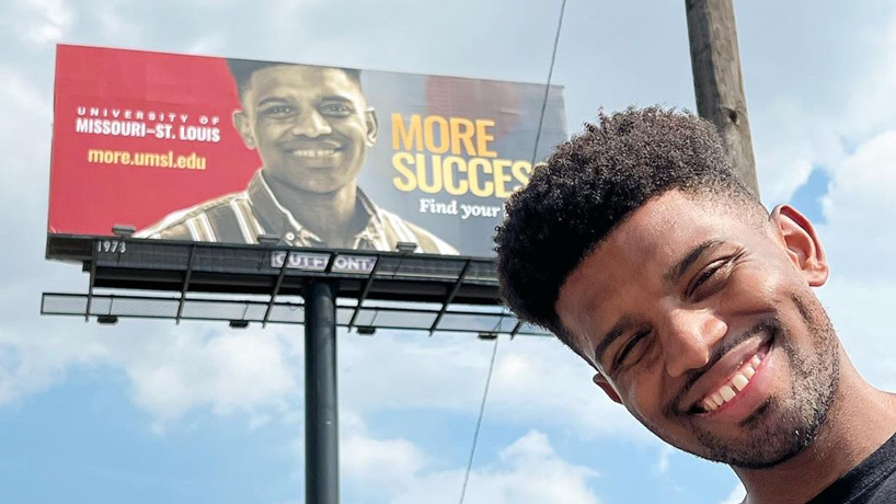 UMSL graduate Brandyn Chambers takes a photo of himself near an UMSL billboard containing his likeness