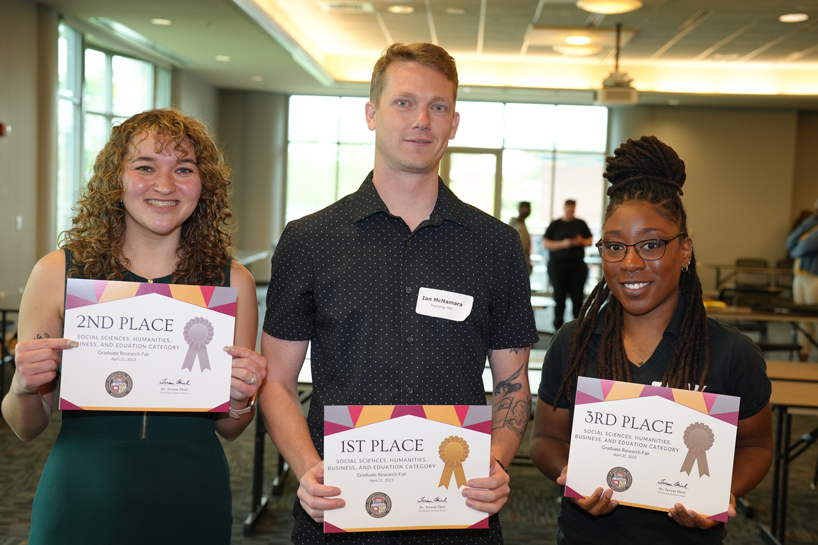 Caitlyn Harriman, Ian McNamara and Kanila Brown hold up their certificates for placing in the top three in the Graduate Research Fair's Social Sciences, Humanities, Business and Education category