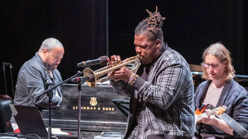 Keyon Harrold plays the trumpet on stage in an auditorium with his band.