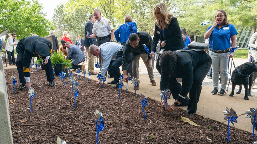 Attendees of an event commemorating Child Abuse Prevention Month plant pinwheels in the garden outside the Kathy J. Weinman Centre