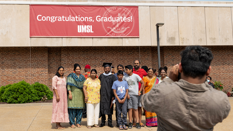 Indian man poses for a photo with his family with a sign in the background that says Congratulations graduates!