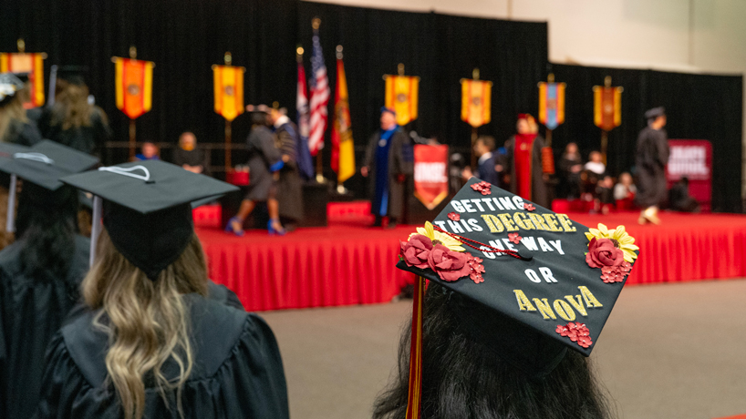 A graduate's cap reads "getting this degree one way or anova" as she prepares to walk to the platform.