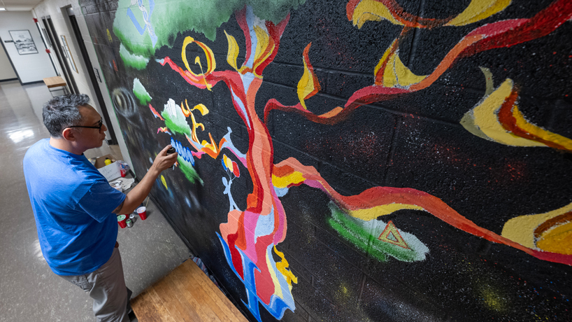 Lantino man touches up mural depicting abstract multicolored tree 