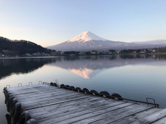 Mount Fuji, snow capped mountain peak, is reflected in the water of a small lake