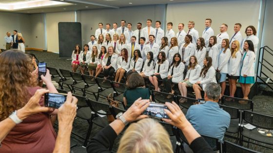 A group of 43 UMSL optometry students pose together with their white coats in the MSC as family members and friends take their picture