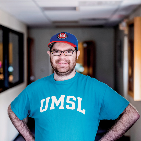 Andrew Holman, white man with glasses in blue and red baseball hat and blue UMSL t shirt