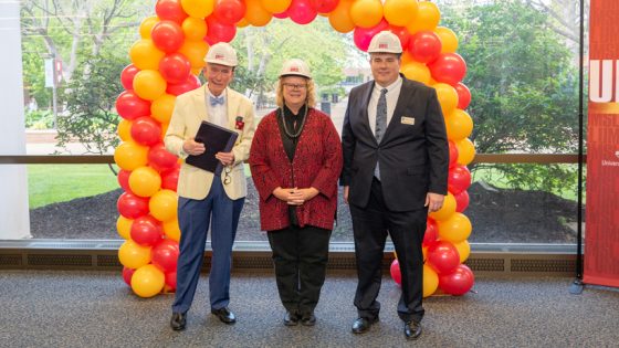 John Neal Hoover, Kristin Sobolik and Christopher Dames don hard hats and stand in front of a balloon arch where the new north entrance to the University Libraries will be built