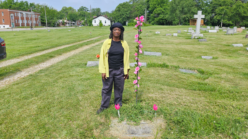 Black woman stands in cemetery at the grave of her great-grandmother.