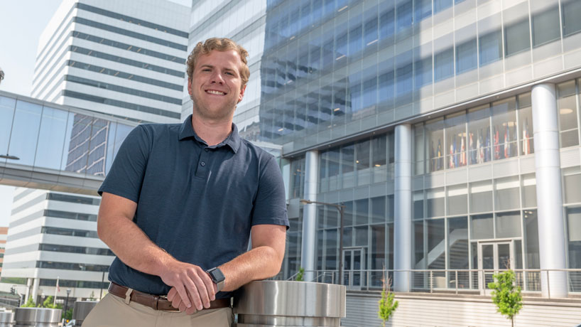 Young white male stands outside in front of a business building.