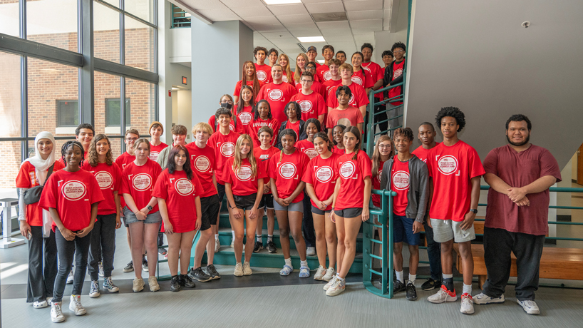 A ground of area high school students wear matching red T-shirts and gather on the steps inside Express Scripts Hall for a photo during the inaugural UMSL Geospatial Summer Camp